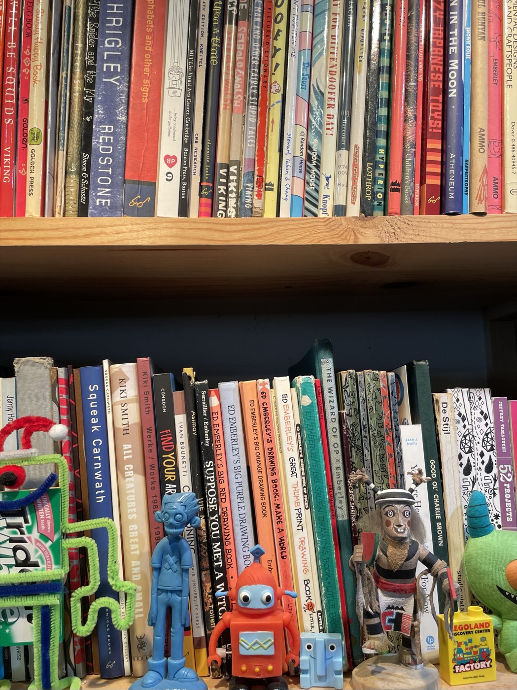 A bookshelf of illustration books with small toy figures